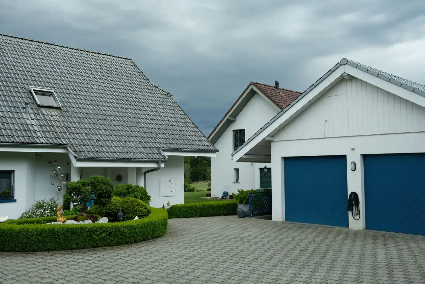 Allée de garage en pavés autobloquants desservant deux maisons individuelles, bordée de haies taillées